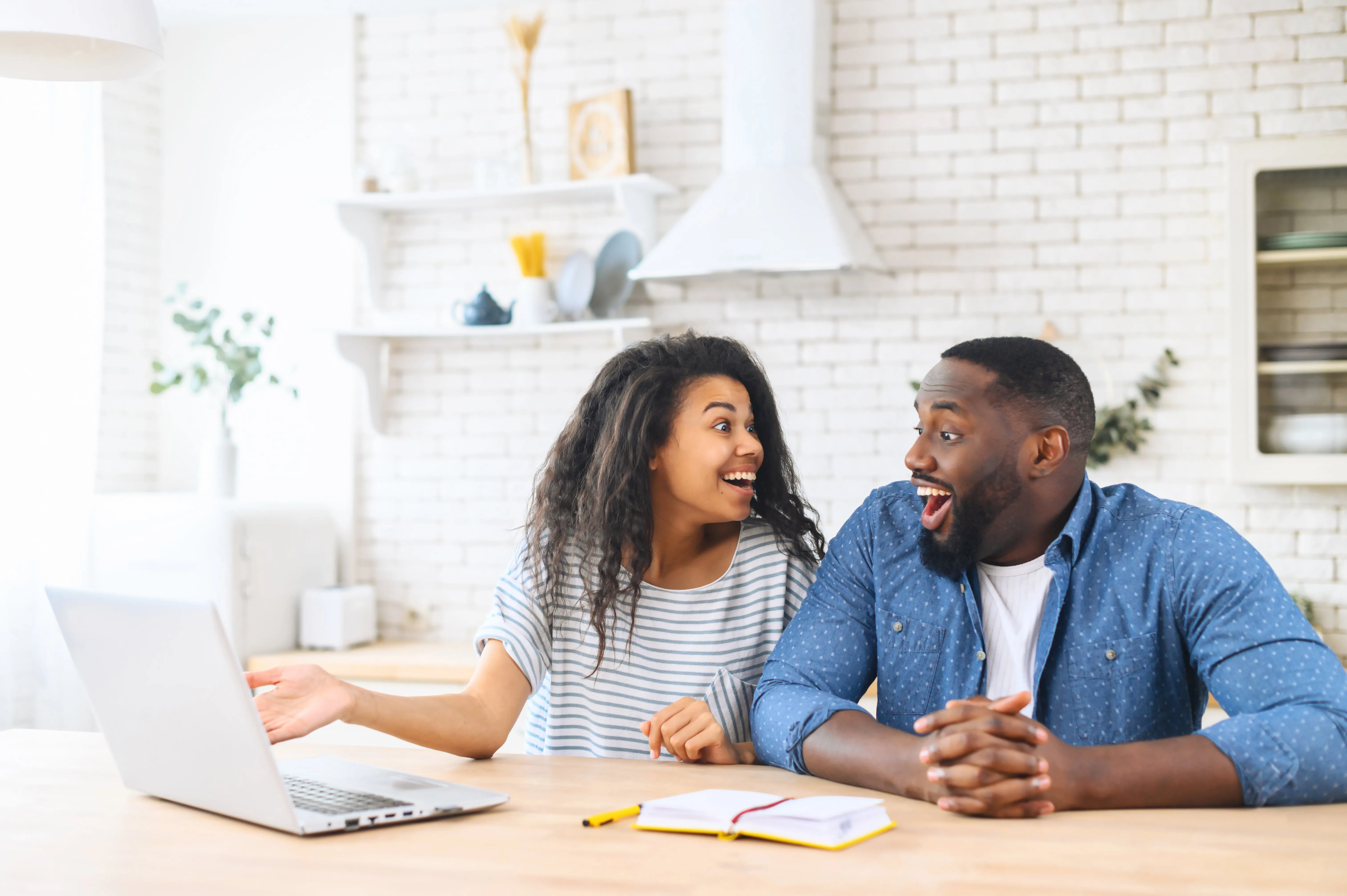 a happy couple looking at each other in front of their laptop