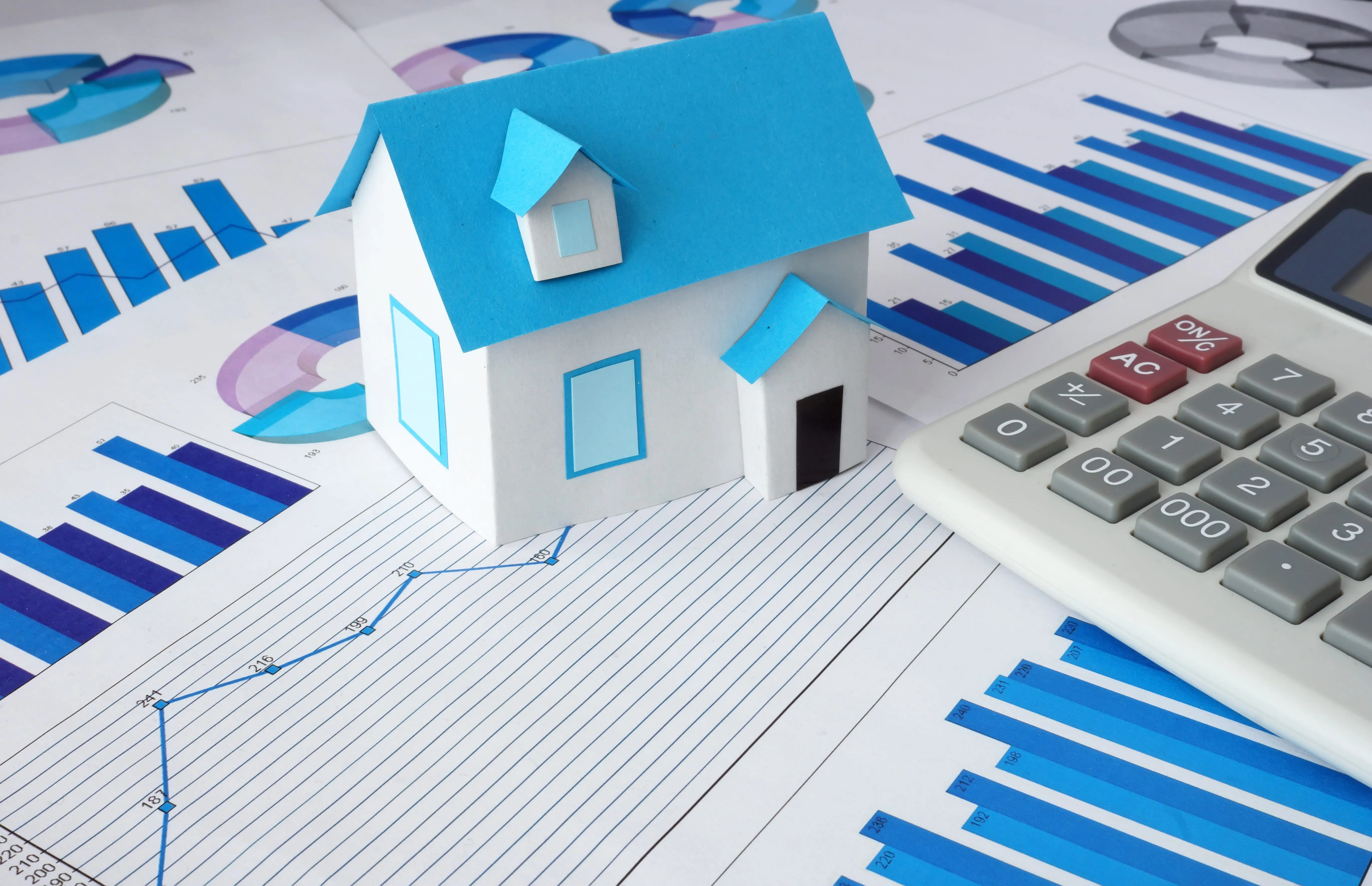 a small house made of paper next to a calculator on other papers that look like reports. 