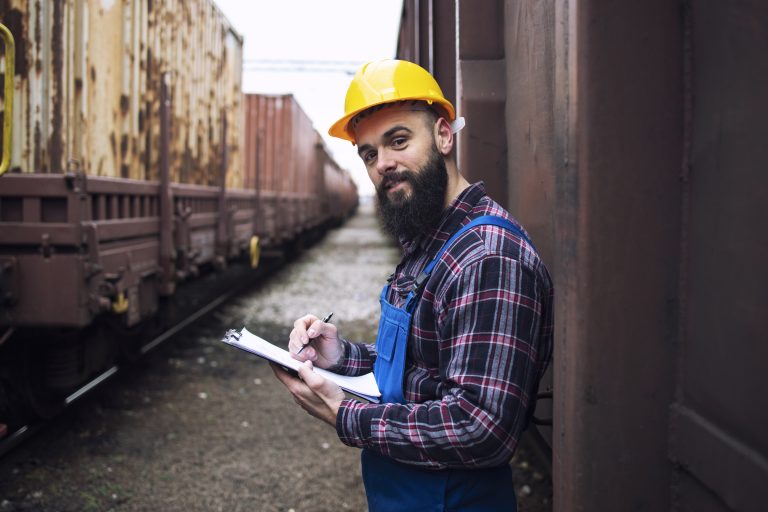 Railroad worker with clipboard standing by the shipping containers and looking to the camera